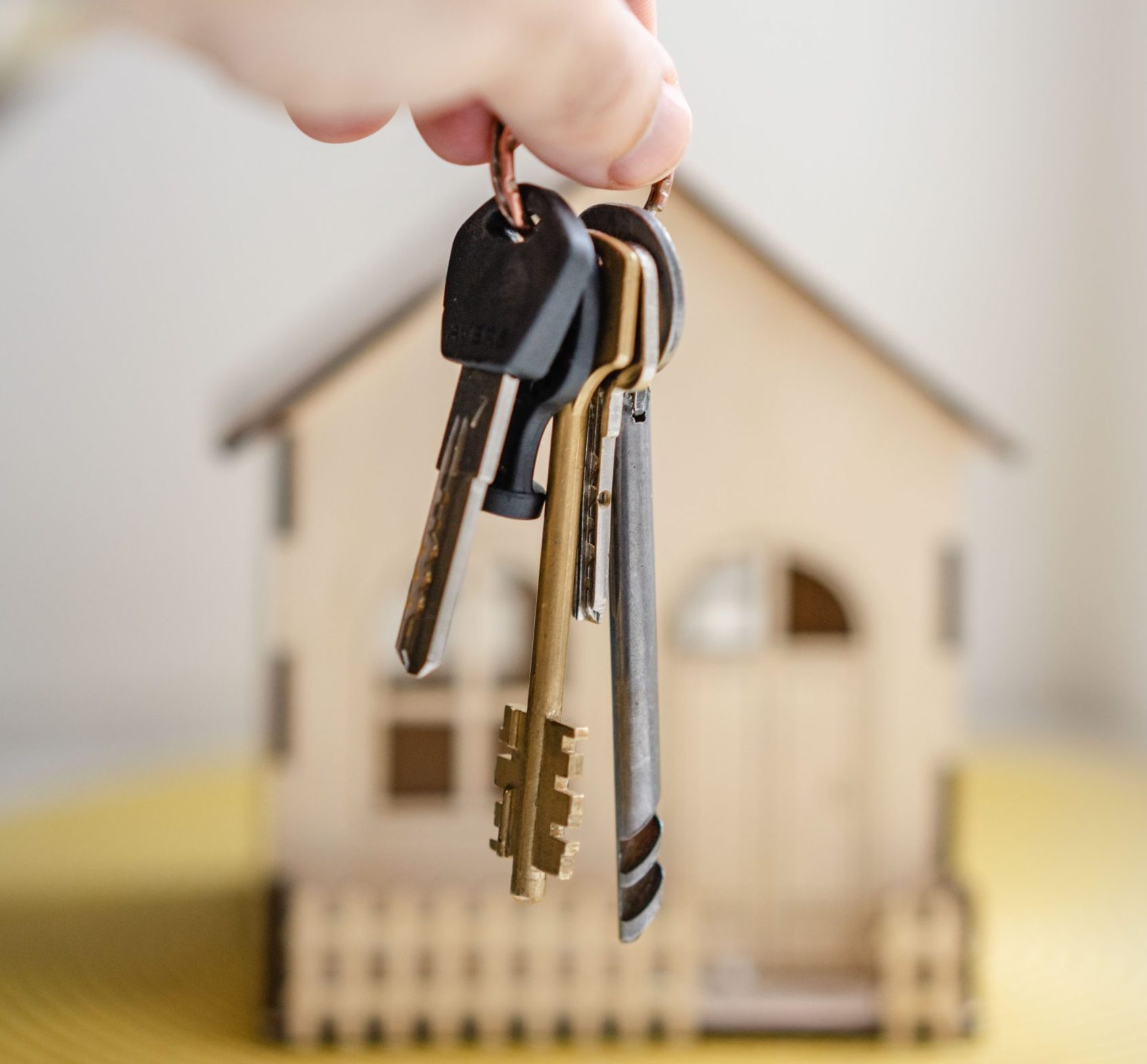 a blurred image of a house with a hand holding a set of keys in front of it.