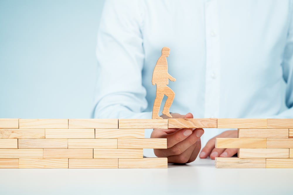 wooden man walking over wooden bridge being held up by a hand